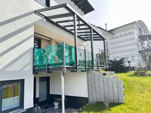 Glasüberdachung mit anthrazitfarbenen Profilen über einer erhöhten Terrasse am Haus